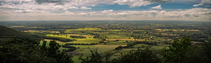 Panoramic view of patchwork farmland and villages from a hillside, under a cloudy sky.