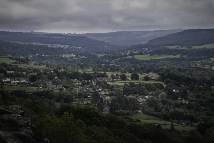 Village nestled in a green valley with rolling hills and patchwork fields under a cloudy sky